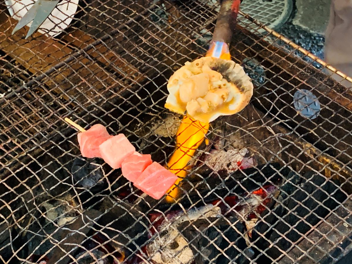 築地三宅水産の店頭でホタテとマグロ串をバーナーで香ばしく炙る様子
